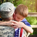 A soldier father is hugging his son holding an american flag outside for a family reunion or 4th of July concept.